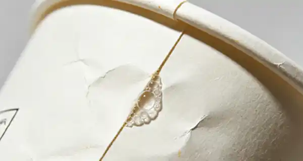 A close-up of a discarded cup that leaks air from its side seam